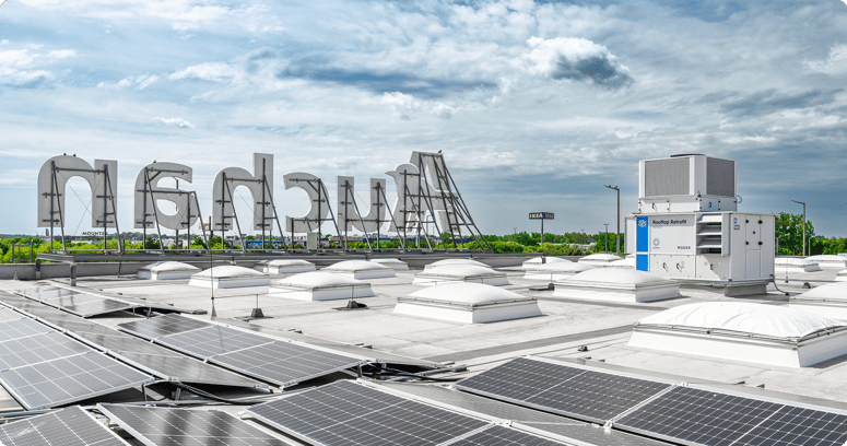 Dak van een Auchan-vestiging met zonnepanelen, daklichten en een witte Rooftop Retrofit IntrCooll-unit. Op de achtergrond het grote Auchan-logo.
