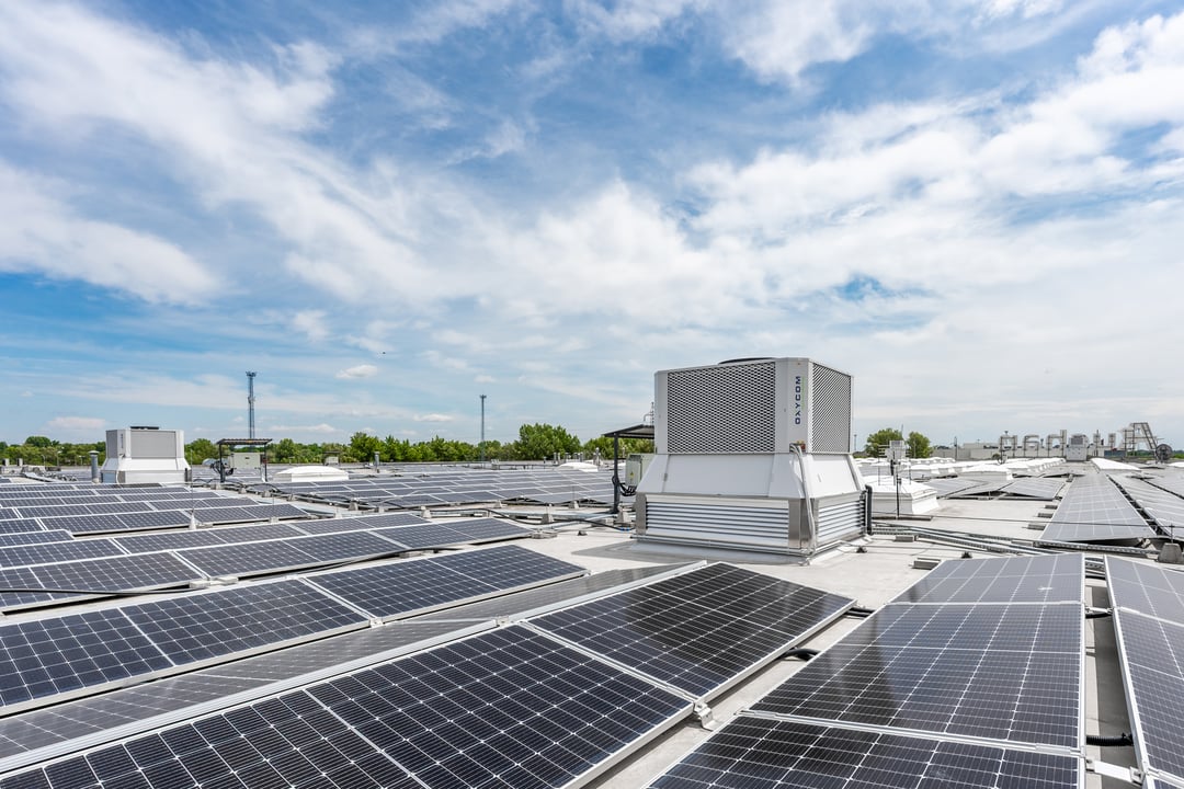 Plat dak van een commercieel gebouw bedekt met zonnepanelen, met een grote IntrCooll-unit in het midden en bomen op de achtergrond.